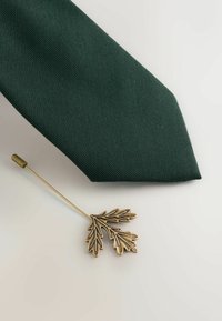 Zaļš teksturēts kaklasaite ar norādītu galu, ko papildina bronzas lapu formas kaklasaite pin no sarežģītas izstrādes.