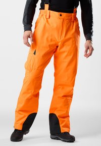 Oranje waterdichte broek met verstelbare banden, zwarte verstevigde manchetten, meerdere zakken en een duurzame stof voor buitensportactiviteiten.
