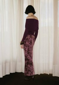 Haut violet décolleté avec un col drapé, associé à une longue jupe violette à motifs. Accentué par une ceinture dorée et des talons noirs.