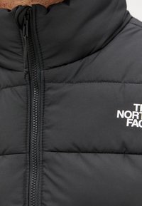 Schwarze Daunenjacke mit hohem Kragen, durchgehendem Reißverschluss, gesteppter Textur und weißem Logo auf der Brust. Weiches, isoliertes Material.