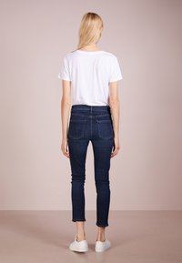 Bílá tričko s krátkým rukávem v kombinaci s tmavě modrými skinny džíny, končícími těsně nad kotníkem, obuté s bílými teniskami. Minimalistický design.