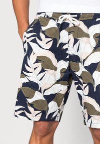 Shorts bleu marine avec un motif feuillu en nuances de vert, rose et blanc ; taille élastique avec cordon de serrage ; poches latérales.