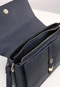 Navy leather handbag with a textured exterior, featuring a zippered interior pocket, gold hardware, and a magnetic snap closure.