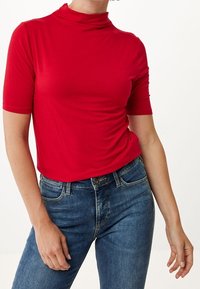 Röd kortärmad polotröja i ett mjukt, stretchigt material, tillsammans med blå denim jeans. Passformen är avslappnad och framhäver den avslappnade stilen.