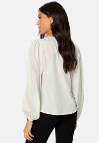Blusa bianca con tessuto testurizzato, maniche a sbuffo e scollo rotondo. Abbinata a leggings neri per un look completo.