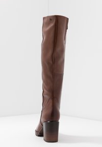 Bottes marron jusqu'au genou en cuir lisse, avec un bout arrondi, des détails de coutures subtils et un talon empilé.