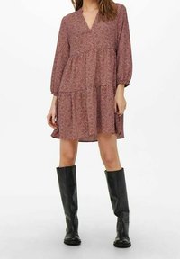 Vestido rojo y blanco con estampado, escote en V, mangas tres cuartos y un diseño de falda en capas, combinado con botas negras hasta la rodilla.