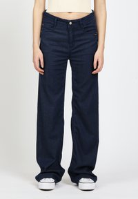 Dunkelblaue Jeans mit weitem Bein aus Denim, ausgestattet mit einem klassischen Fünf-Taschen-Design, Metallknopfverschluss und minimaler Markenkennzeichnung auf der Vorderseite.