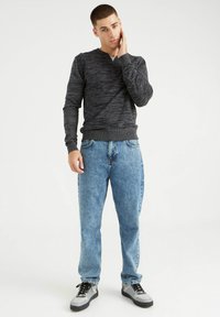 Camisa henley de manga larga negra texturizada, jeans ajustados de color azul claro y zapatillas grises con acentos negros. Atuendo casual exhibido en un modelo masculino.