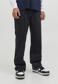 Svart denimbyxor med lös passform, featuring stora cargofickor och en blekt textur. Matchas med svarta och vita sneakers.