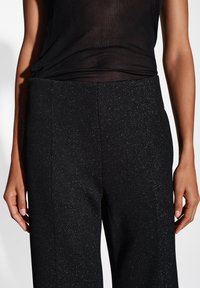 Zwarte geribde broek met een subtiele glans, voorzien van een elastische tailleband en een rechte pijp. Soepele textuur en geen zichtbare hardware.