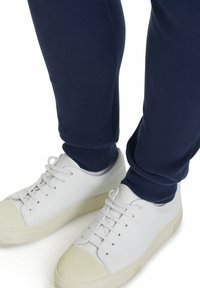 Marineblauwe sweatpants met geribbelde boorden, gecombineerd met witte leren sneakers met een ronde neus en platte rubberen zool, voorzien van vijf oogjes.