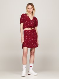 Röd blommig crop top med puffärmar och knutdetalj; matchande kjol har en volangkant. Modellen bär vita sneakers och strumpor.