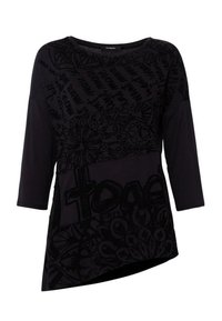 Svart långärmad asymmetrisk topp med blandade abstrakta och blommiga mönster samt delvis fet text på framsidan.
