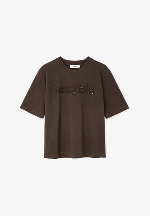 T-shirt marron à manches courtes en coton, arborant le mot "tassollato" brodé en fil sombre avec des rivets décoratifs.