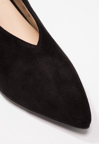 Chaussure plate en daim noir à bout pointu avec une empeigne basse et une doublure intérieure beige sur fond blanc.