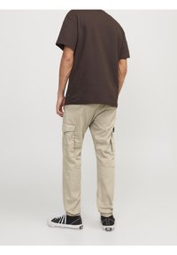 Brązowa koszula z krótkim rękawem, khaki spodnie cargo z wieloma kieszeniami, czarne sneakersy z białymi podeszwami. Prosty, luźny krój.