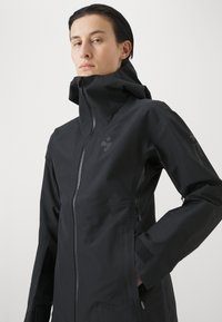 Schwarze wasserdichte Jacke mit hohem Kragen, Frontreißverschluss, verstellbaren Manschetten und Logodetail am Ärmel. Strukturierter, eleganter Design.