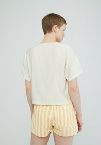 Crème kortemouwtop met een vierkante halslijn en een iets gestructureerde stof, gecombineerd met geel-witte gestreepte shorts met zijzakken.