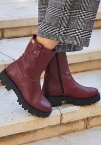 Botas de piel burdeos hasta el tobillo con puntera redonda, cremallera lateral y suela de goma con un patrón de adherencia; incluye una pequeña pestaña en el collar.