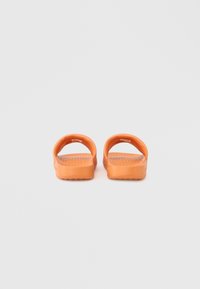 Πορτοκαλί λαστιχένια σανδάλια με φαρδιά λουρά, υφασμένο πάτο και ραβδωτή σόλα. Διαθέτουν λείο φινίρισμα και κυκλικό σχεδιασμό με κοψίματα.