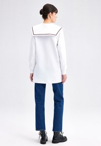 White sweatshirt dress with a large, contrasting collar and long sleeves, paired with blue straight-leg jeans and black lace-up boots.
