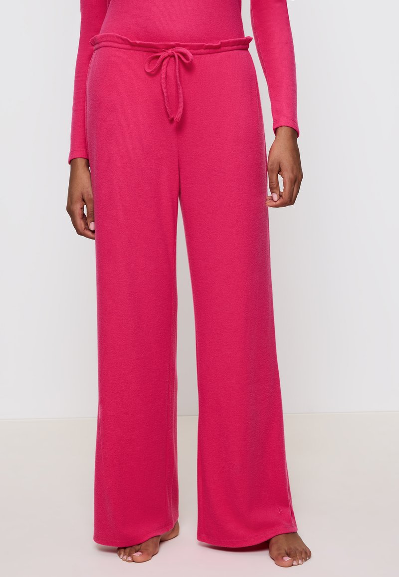Roze loungewear broeken gemaakt van zachte stof, met een relaxte pasvorm, wijde pijpen en eenוסטרingtaille met een simpele knoopdetail.