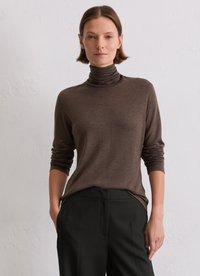 Een bruine coltrui van zacht materiaal, met lange mouwen en een relaxte pasvorm, gecombineerd met zwarte broek.
