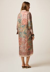 Een lange, bloemenpatroon jurk in levendige kleuren van roze, blauw en groen, met een zachte textuur en een losse pasvorm. Heeft een kraag en lange mouwen.