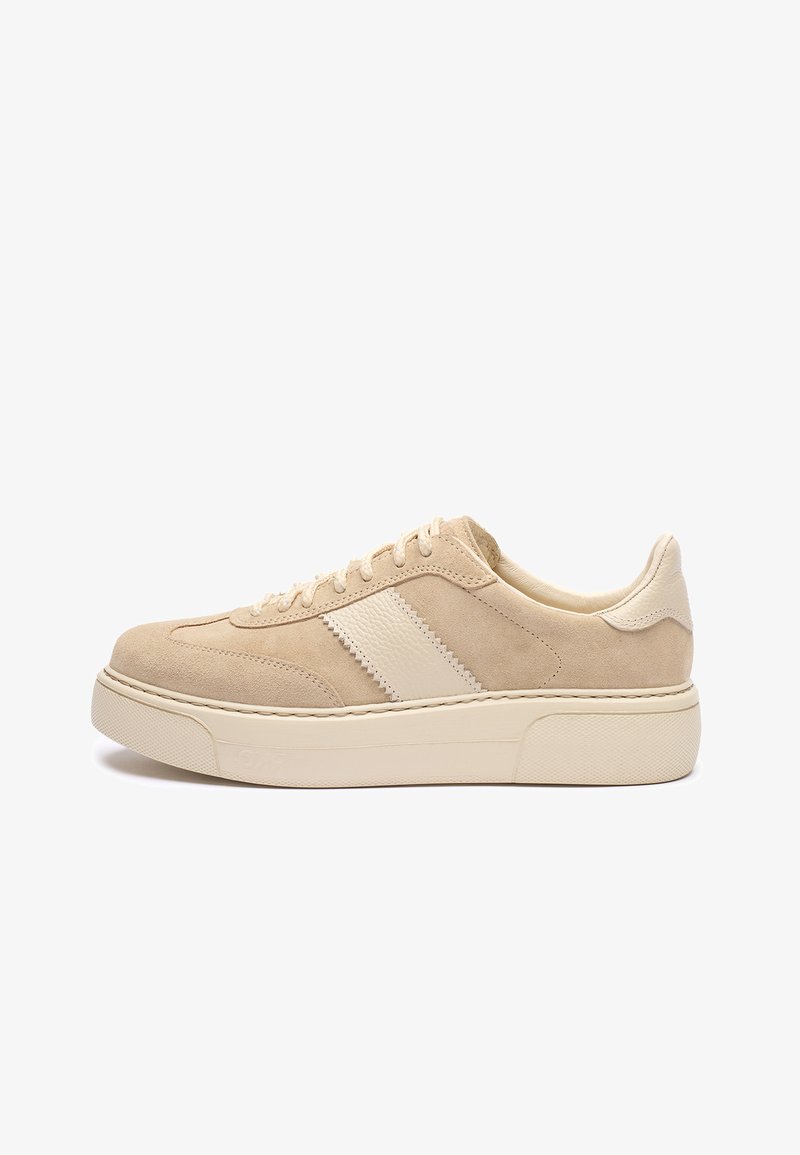 Beżowy zamszowy trampki z teksturowanym białym skórzanym paskiem, okrągłym noskiem i grubą kremową gumową podeszwą. Sznurowadła i przeszycia są w kolorze beżowym, dopasowane.