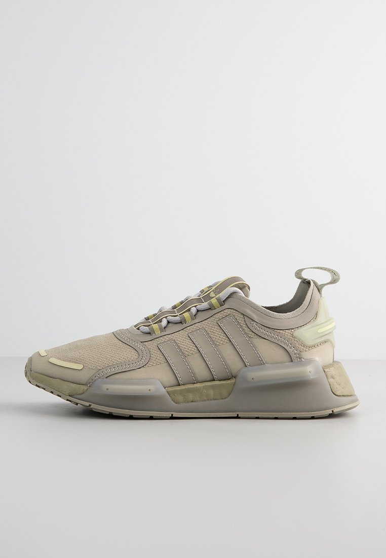 Zapatillas sintéticas beiges con acentos en gris, parte superior texturizada, tres franjas en el lateral y suela gruesa. Presenta cordones elásticos y tira en el talón.