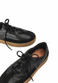 Mustat nahka- ja mokkanahkakengät pyöreällä kärjellä, tasapohjaisella ruskealla kumipohjalla ja mustilla nauhoilla, joissa on teksturoitu päällinen.