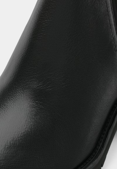 Bottine en cuir noir avec une texture lisse et une forme arrondie, présentant des coutures discrètes et une semelle en caoutchouc durable.