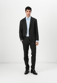 Black suit jacket with a tailored fit, paired with a light blue button-up shirt and matching trousers. Glossy black shoes complete the look.