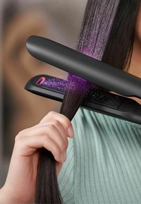 Lisseur à cheveux noir glissant sur des cheveux lisses et sombres. Présente un embout vapeur avec une lumière violette, des surfaces lisses et un design élégant.
