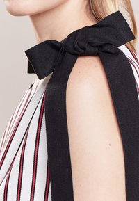 Detailní záběr na rameno v bezramínkovém pruhovaném topu, který je na rameni uvázán velkou černou mašlí.