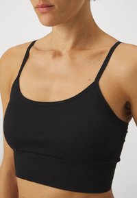 Črn rebrast crop top z tankimi naramnicami, ki ima prilegajoč dizajn in brezšivno konstrukcijo, poudarja gladko teksturo in jasne linije.