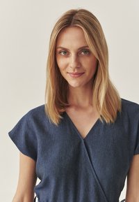 Jeans Wickelkleid, kurze Ärmel, tiefer V-Ausschnitt, strukturierter Stoff, in Dunkelblau, mit einem taillierten Bund und Bändern an den Seiten.