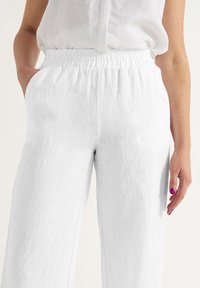 Witte linnen broek met een elastische tailleband, ruime pijpen en zijzakken. De stof heeft een lichte, gestructureerde uitstraling.