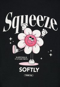 Schwarzes T-Shirt mit einem rosa Cartoon-Blumencharakter, der lächelt, die Arme hebt und mit weißem Text "Drücke" und "Glück ist in allem".