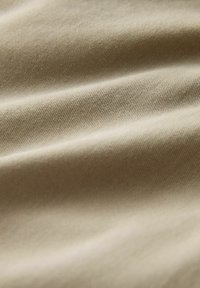 Close-up of beige fabric with diagonal weave texture and soft shadows highlighting its folds.