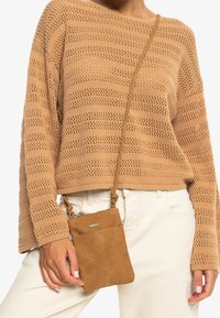 Stickad tröja i ljusbrun med öppen väv och horisontella ränder. Beige axelremsväska med dragkedja, bärs över kroppen.