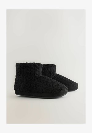 Zwarte, gestructureerde, gebreide sloffen met een met bont gevoerde rand en een platte rubberen zool, ontworpen voor comfort en warmte in binnenruimtes.