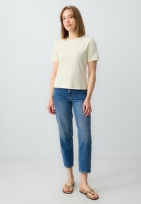 Lichtbeige korte mouwen t-shirt gecombineerd met blauwe cropped jeans. Het shirt heeft een ronde halslijn en de jeans hebben een vervaagde textuur.