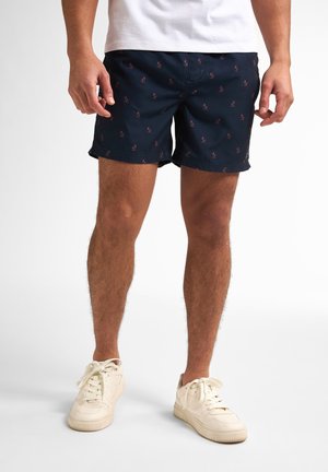 Costumi da bagno blu navy con un motivo ripetuto di piccoli fenicotteri rosa, realizzati in tessuto leggero, con un taglio classico e tasche laterali.