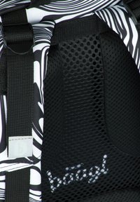 Zaino a fasce bianche e nere con imbottitura in rete, spallacci intrecciati e un'etichetta con il logo "b". Superfici texture visibili.