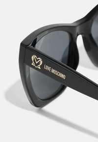 Occhiali da sole neri con montatura angolare, lenti scure e logo "Love Moschino" dorato sulla tempia. Texture in plastica liscia con finitura lucida.