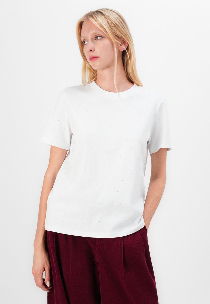 T-shirt bianco con maniche corte, caratterizzato da un colletto rotondo e un motivo a pois in blu chiaro. Il tessuto è morbido e leggero.