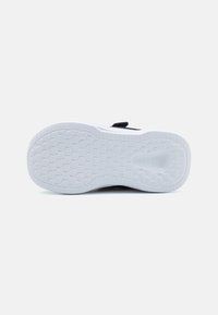 Semelle en caoutchouc blanche avec un motif de grip texturé, présentant une section supérieure noire et un accent rouge près du talon. Design épuré.