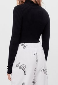 Svart ribbad långärmad topp i kombination med vita byxor med mönster av svarta ormar och elastisk midja. Toppen har en hög halsringning.